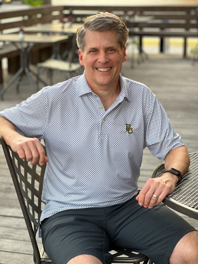 man wearing peter millar polo with BU on it sitting in a chair on a patio