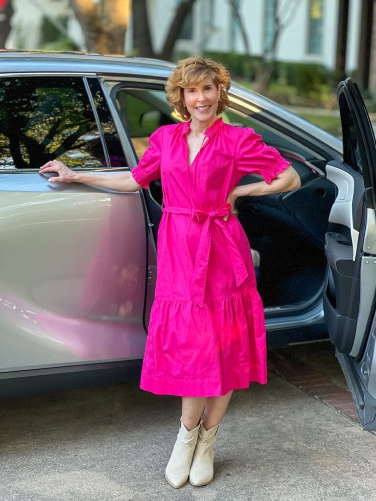 woman over 50 wearing fall transition dress in pink standing by a silver car