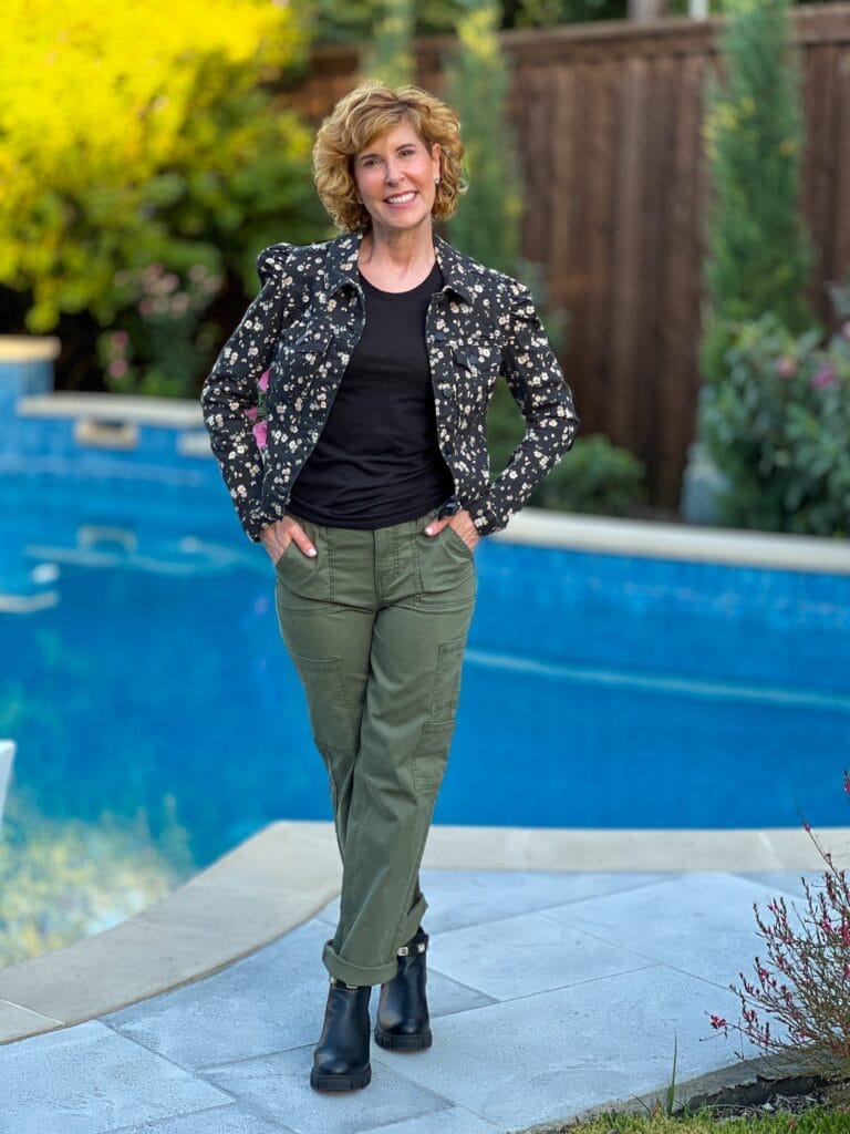 woman standing by a pool wearing green cargo pants, a black tee and a black floral denim jacket