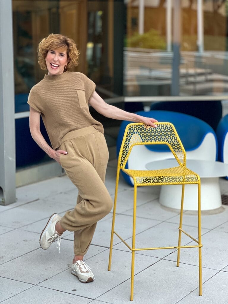 woman standing by a tall yellow chair with one leg bent and hand in pocket wearing a tan 2-piece Amazon set