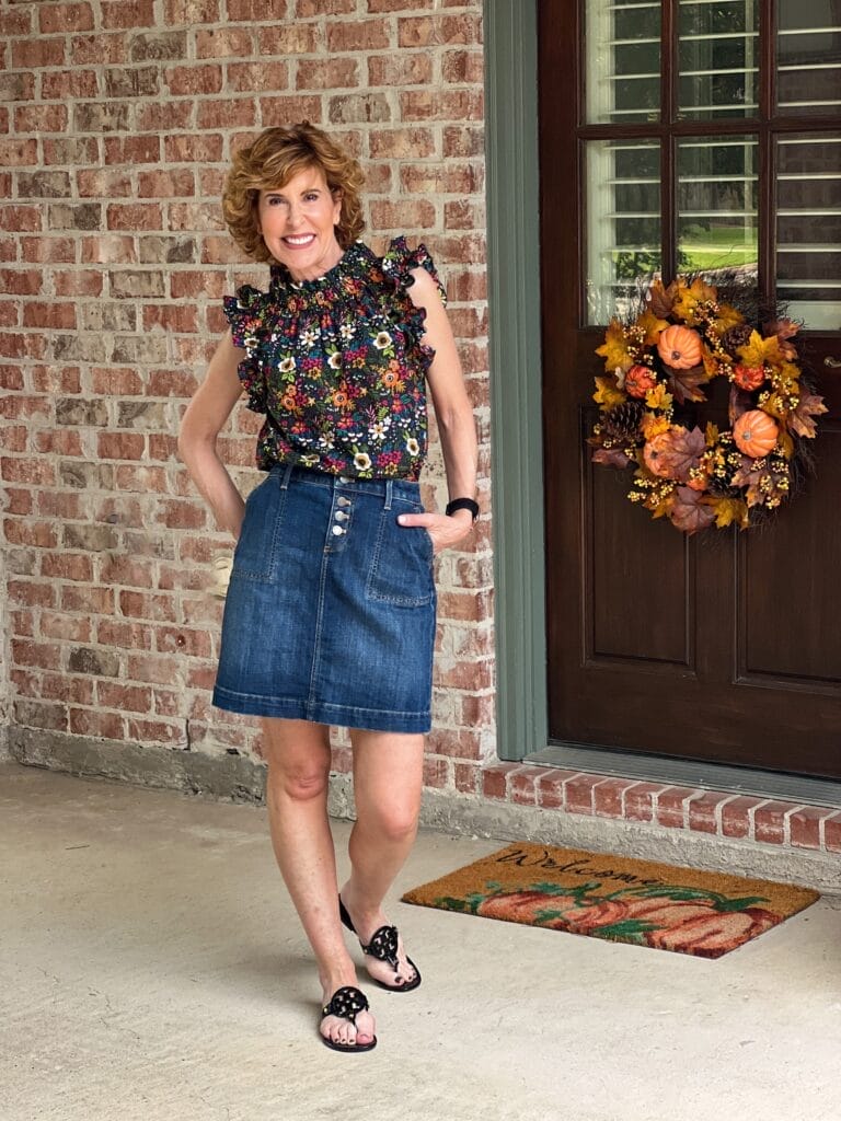 woman standing by back door wearing denim above the knee skirt with avara fall top