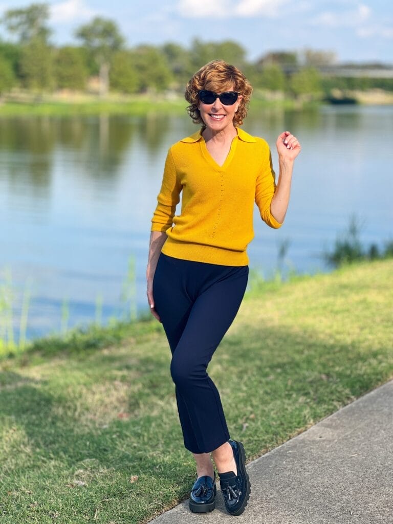 woman standing by river wearing gold 3/4 sleeve sweater with collar and navy pants