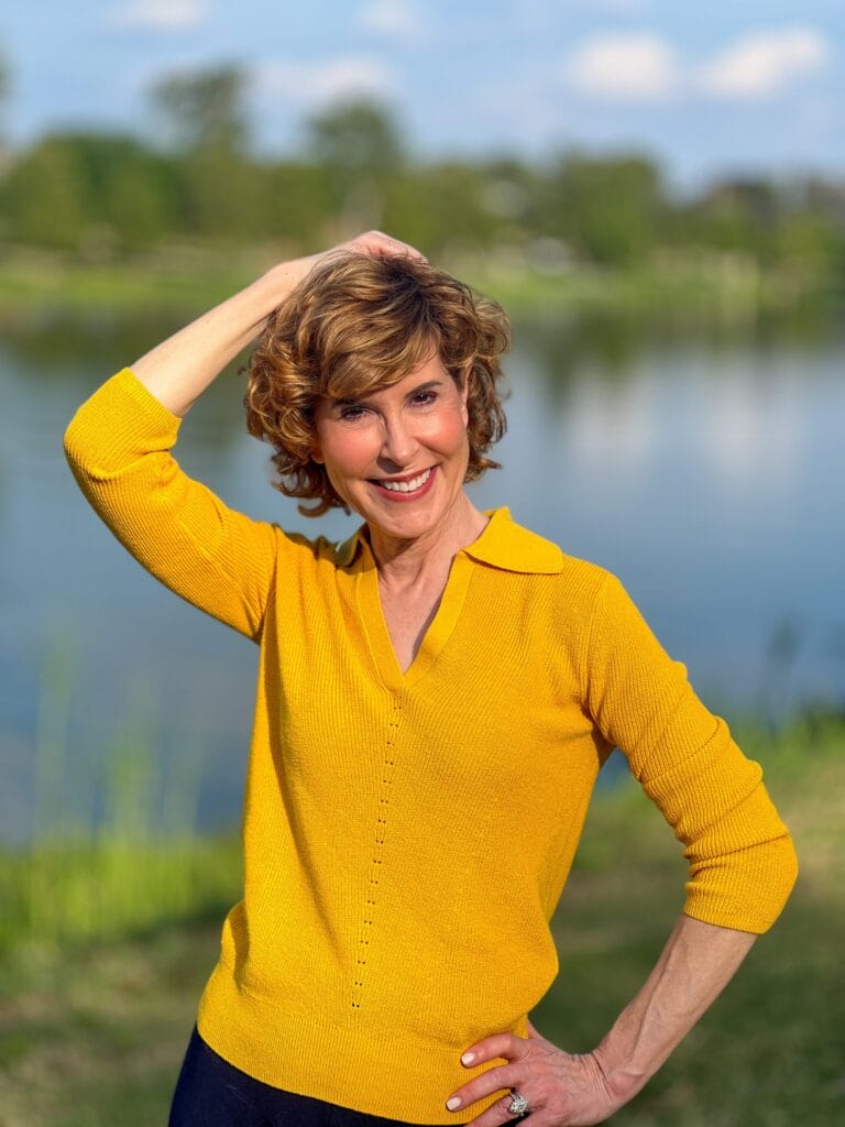 woman wearing gold johnny collar sweater standing by a river