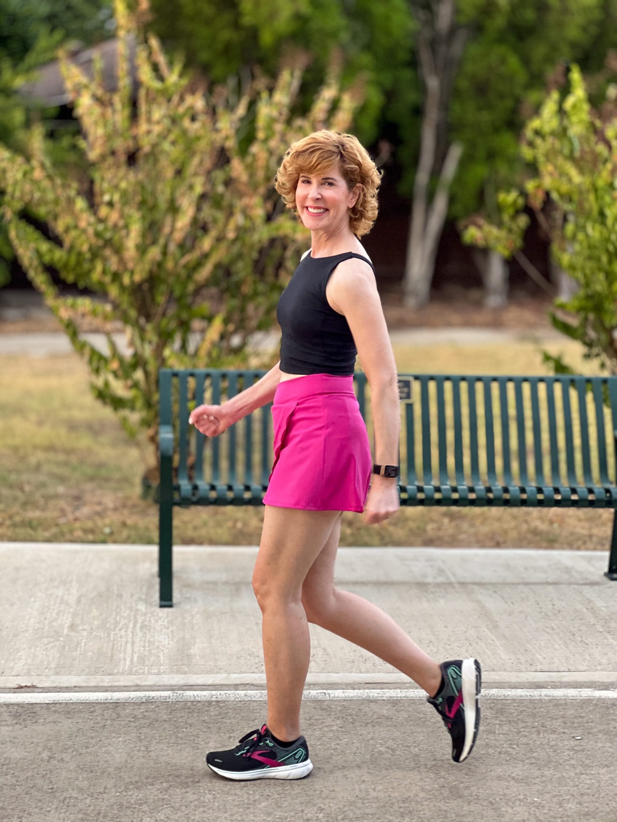 woman over 50 wearing black workout tank and hot pink scallop edge skirt workout wear walking
