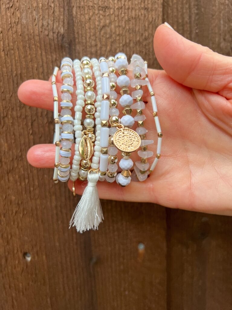 woman's hand holding a white stack of beaded bracelets