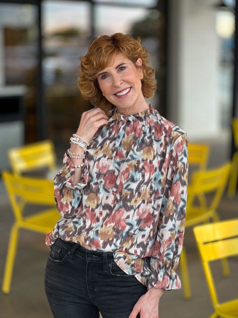 woman wearing fall top standing outside by yellow chairs at a restaurant