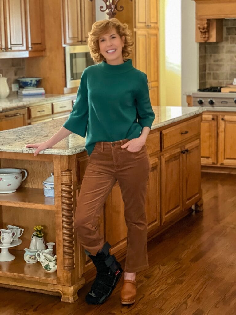 woman wearing avara green sweater and brown cords standing in kitchen