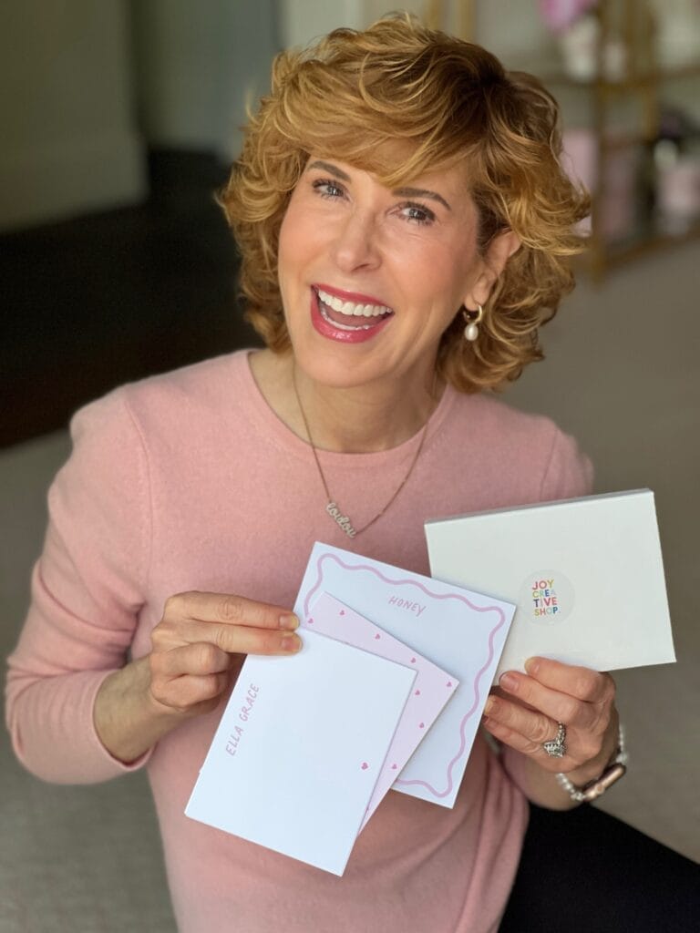 woman in pink sweater sitting on floor holding idea for new grandparent gifts