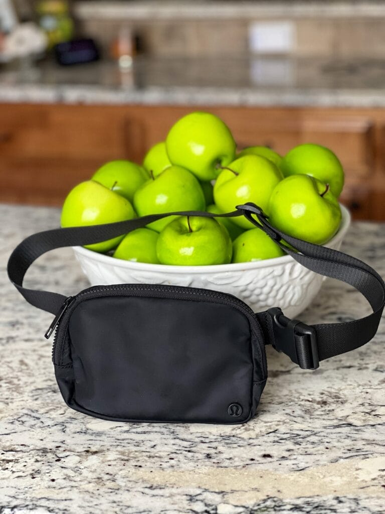 lululemon belt bag in black sitting in front of a white bowl filled with apples