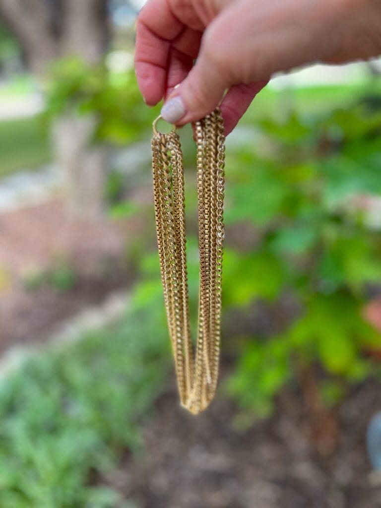 woman's hand holding up cabi dream weaver necklace in gold
