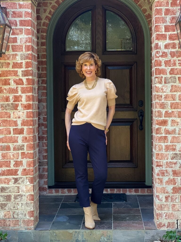 woman standing in front of a front door  wearing amazon puff sleeve taupe sweater and talbots montauk slacks in navy 
