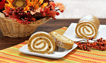 Picture of a pumpkin roll on a plate with autumn flowers behind it