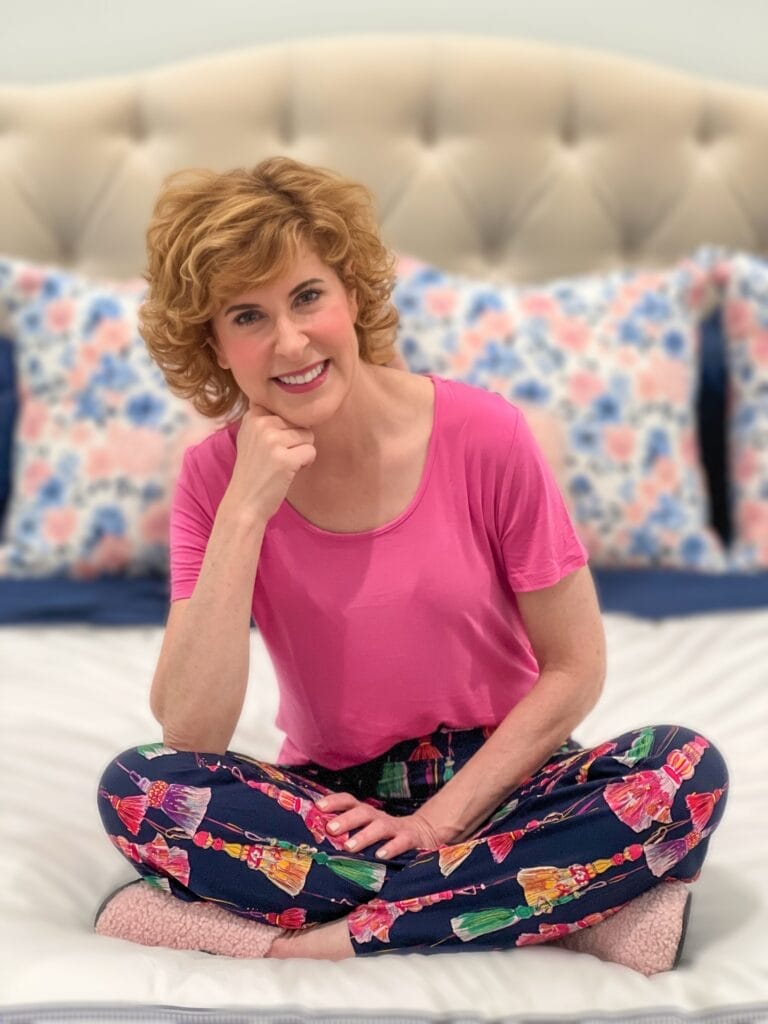 woman sitting cross-legged on a white bed wearing soma cool nights holiday pajamas