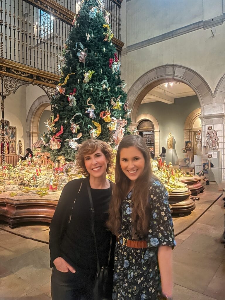 two women standing in front of the baroque nativity scene and tree in nyc at the met museum