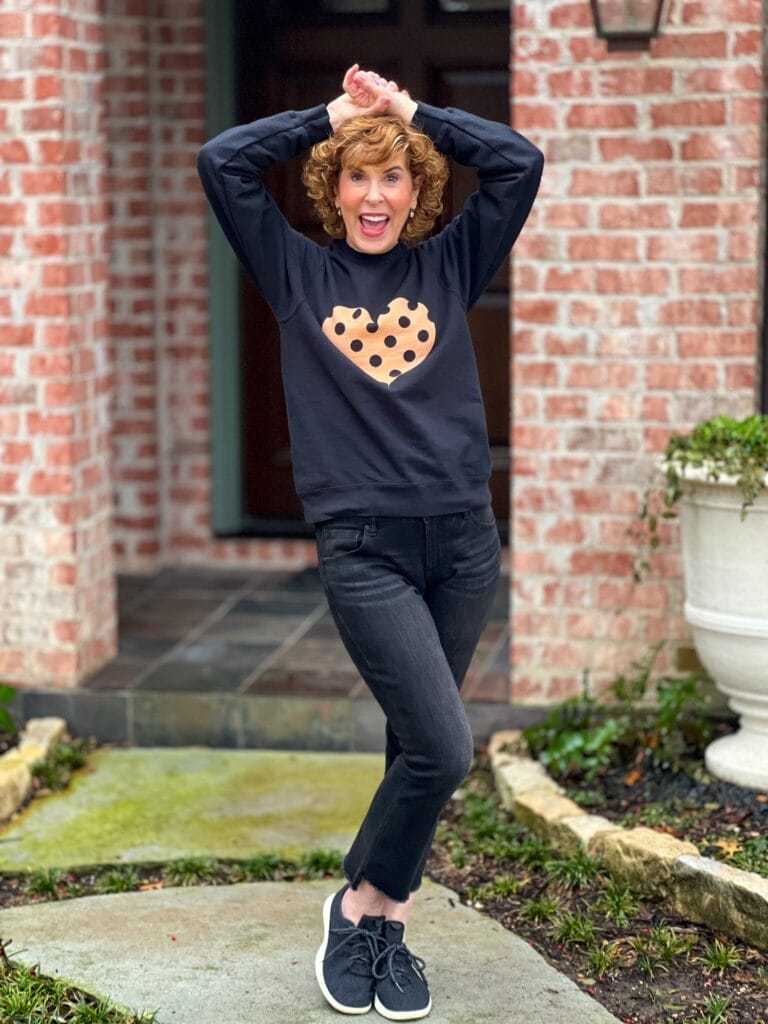 woman standing in front of house wearing black and peach heart sweatershirt