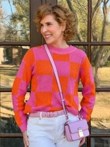 woman over 50 wearing pink and orange sweater from avara standing in front of french doors photographed waist up