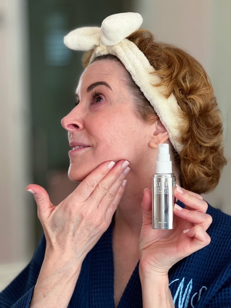 woman over 50 wearing a blue robe and a cream bow headband putting on Ziip silver conducting gel in preparation for using a microcurrent device