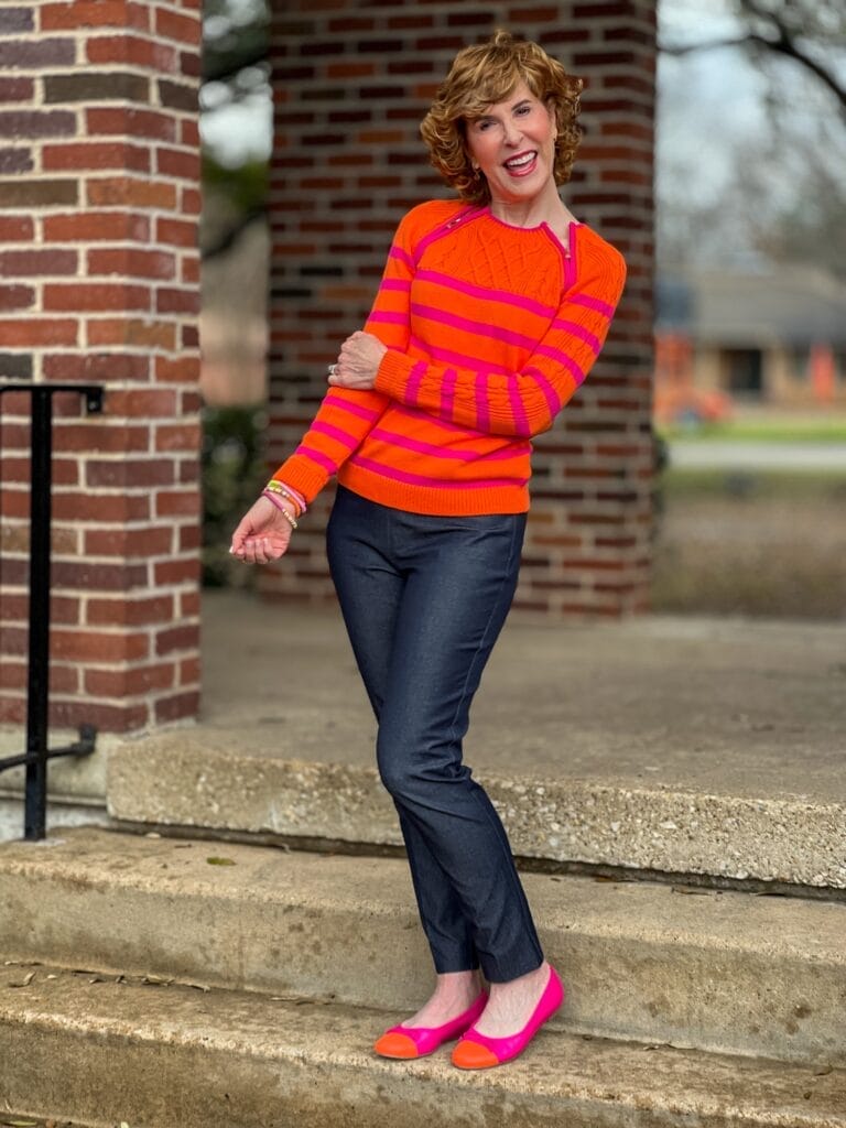 woman over 50 standing on steps wearing orange sweater and denim pants
