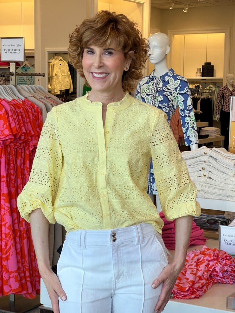woman wearing eyelet yellow top and white pants standing in a talbots store