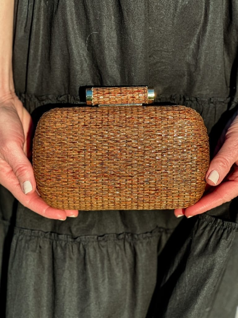 rattan clutch held by woman on background of her black dress