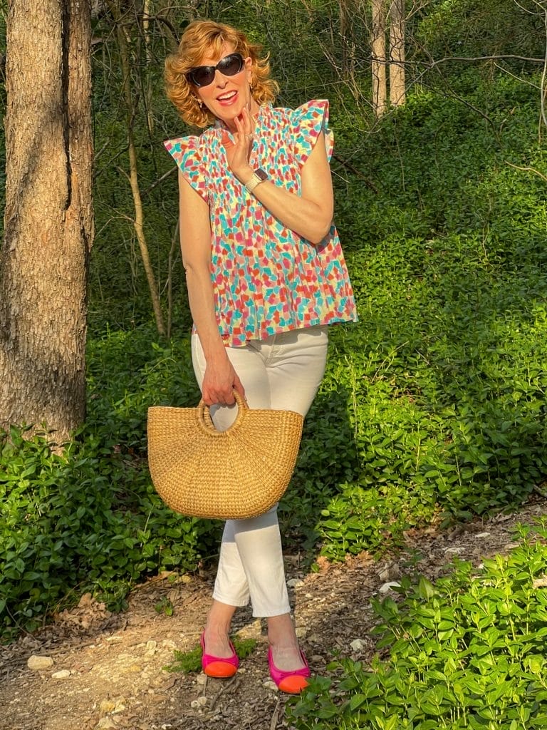 woman standing in the woods in a spring top and white pants holding a summer tote