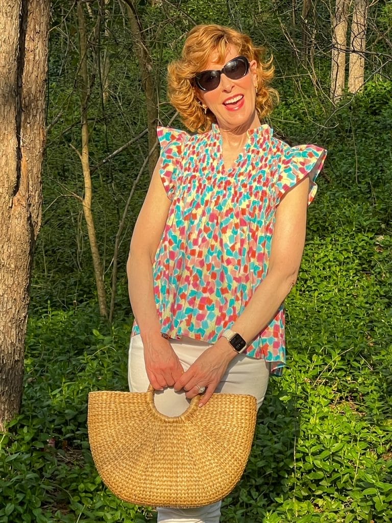 woman in the woods wearing spring colorful top and carrying rattan tote