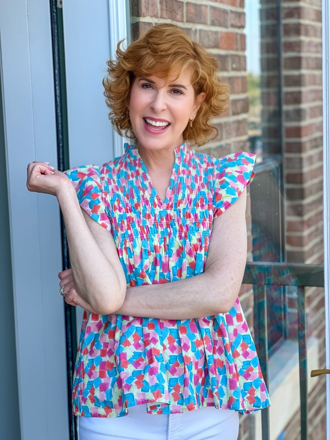 woman over 50 standing outside on a balcony wearing a brightly colored shirt