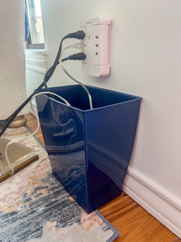 navy blue plastic wastebasket with charging cords coming out the top