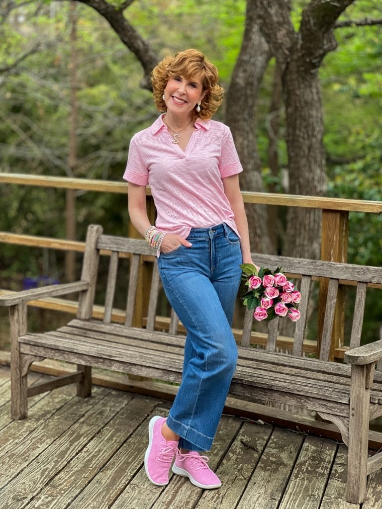 woman standing in front of a bench wearing pink Talbots Johnny collar shirt and wide leg jeans with pink tennis shoes holding pink roses