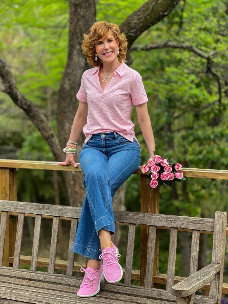 woman wearing pink johnny collar tee and wide leg jeans sitting on a wooden railing