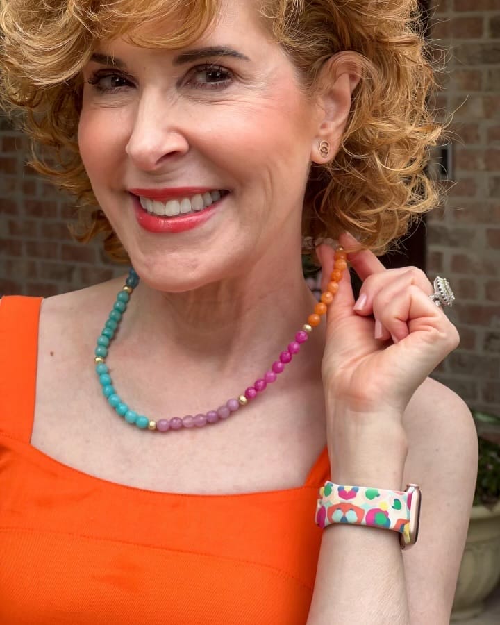 Woman in orange dress showing her multicolored necklace