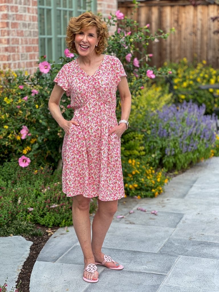 woman standing in backyard wearing a walmart floral dress with flowers behind her in multiple colors