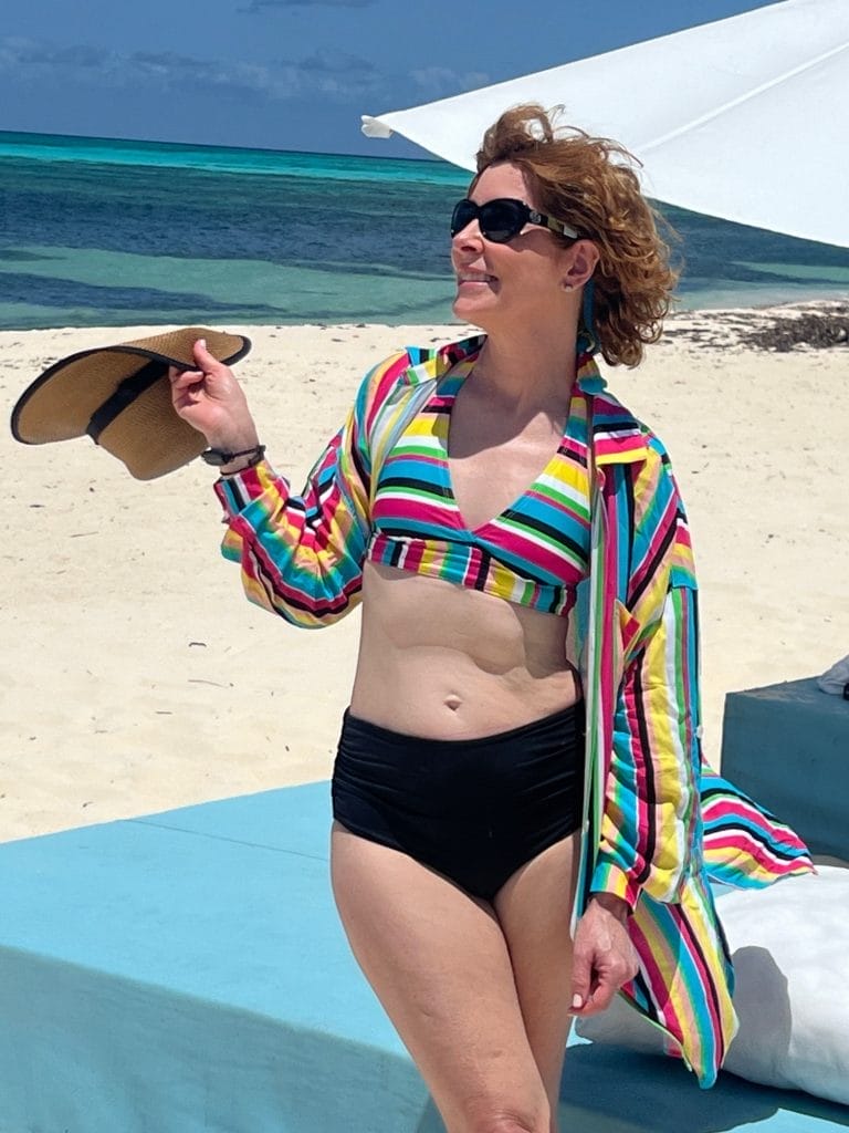 woman standing on a beach wearing a colorful bikini top and black bottoms with a colorful cover up