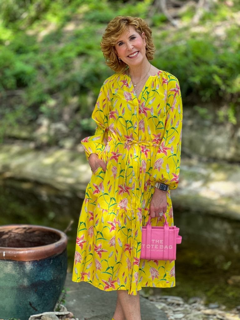 woman standing by a stream wearing a yellow floral dress and carrying a pink purse