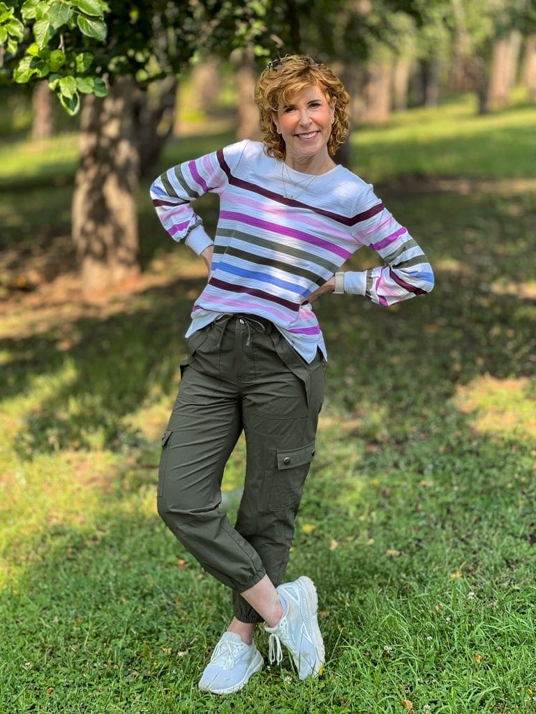 woman over 50 standing in the woods wearing a transitional outfit