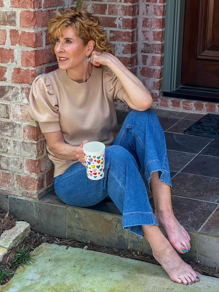 woman with coffee cup with hearts on it sitting on porch looking to the side pensively