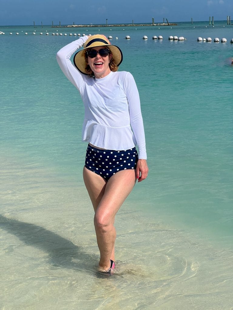 woman standing in the ocean wearing spanx swim shirt and blue and white polka dot high waist bikini bottoms