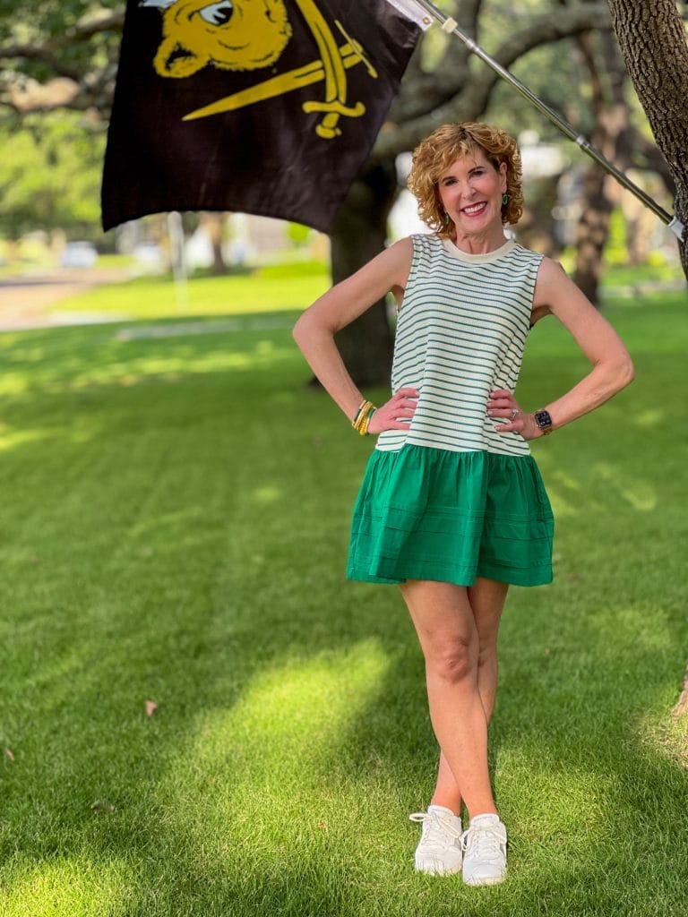 Woman standing in a yard in front of a Baylor flag with a green and white dress on wearing white sneakers