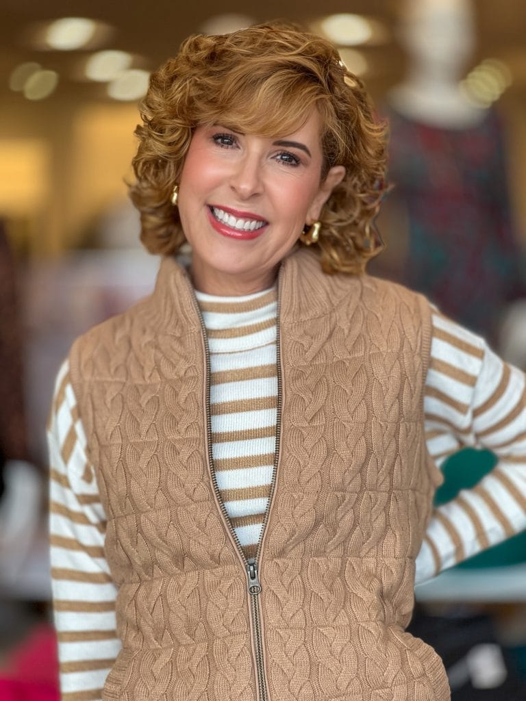 woman wearing gold and white striped sweater with cable knit vest on top