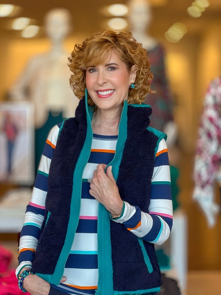 woman over 50 standing in a talbots store wearing blue and whit striped shirt with blue vest on top