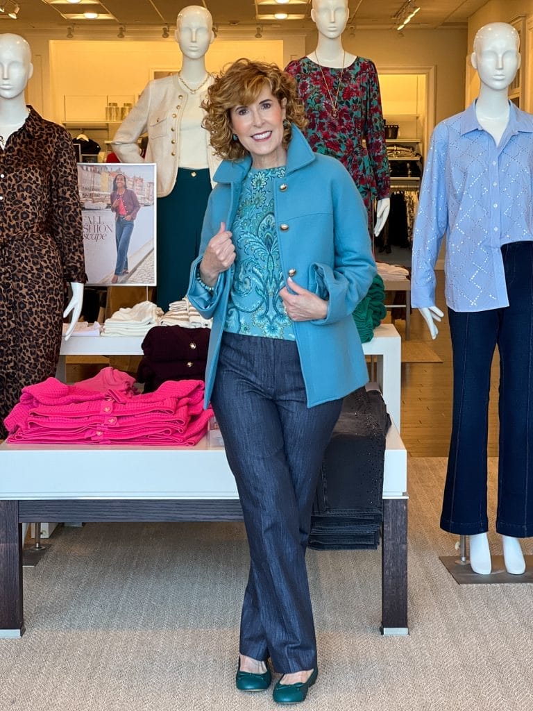 woman over 50 standing in a talbots store wearing blue coat over cashmere blue print sweater and trouser jeans with teal ballet flats