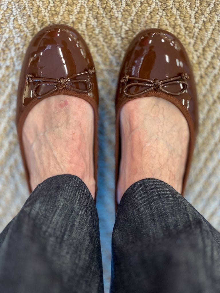 woman's feet wearing brown patent ballet flats