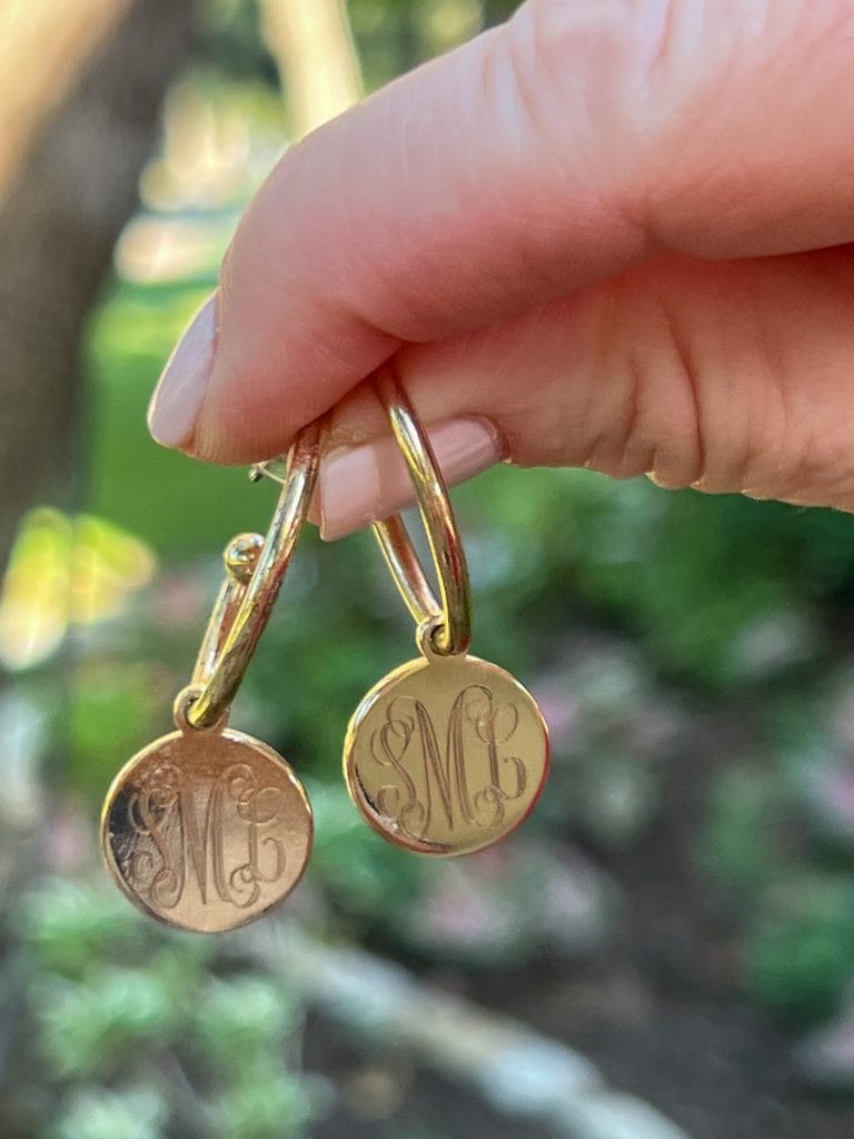 woman's hand holding a pair of monogram hoop earrings