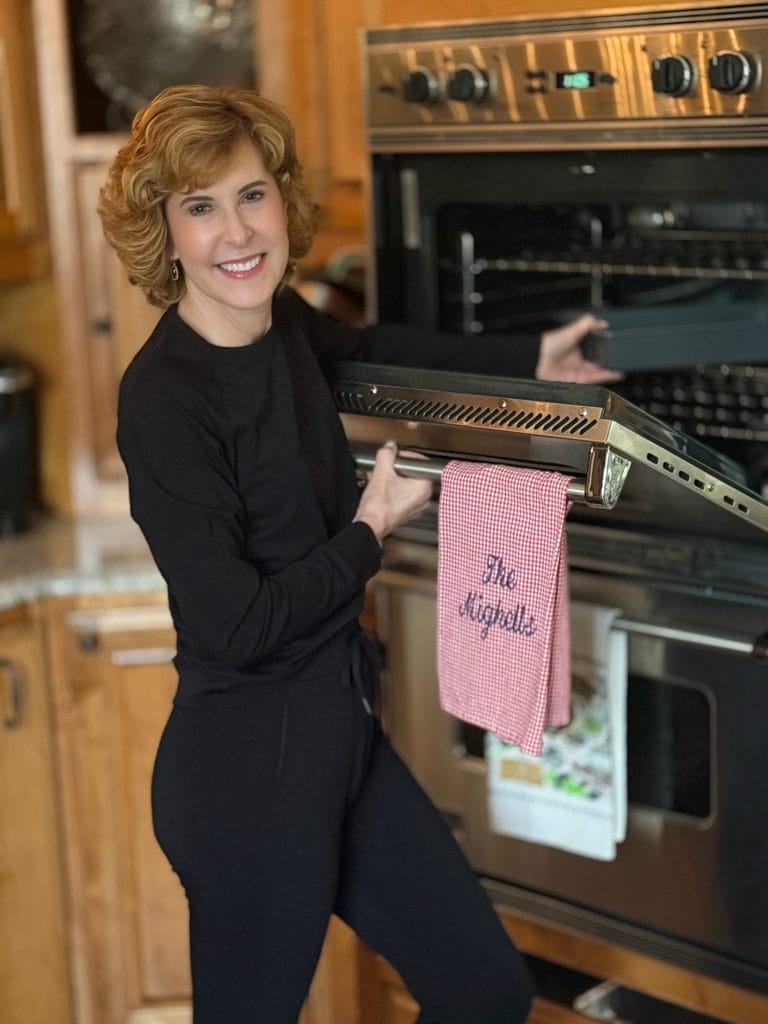 Woman standing in kitchen taking something out of the oven in a black 2 piece cozy earth jogger set.