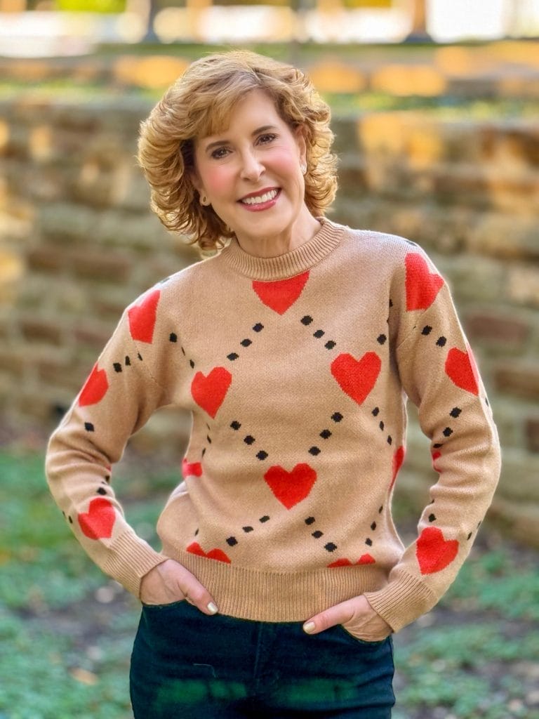 Woman standing outside from waist up in a beige with orange heart fall sweater