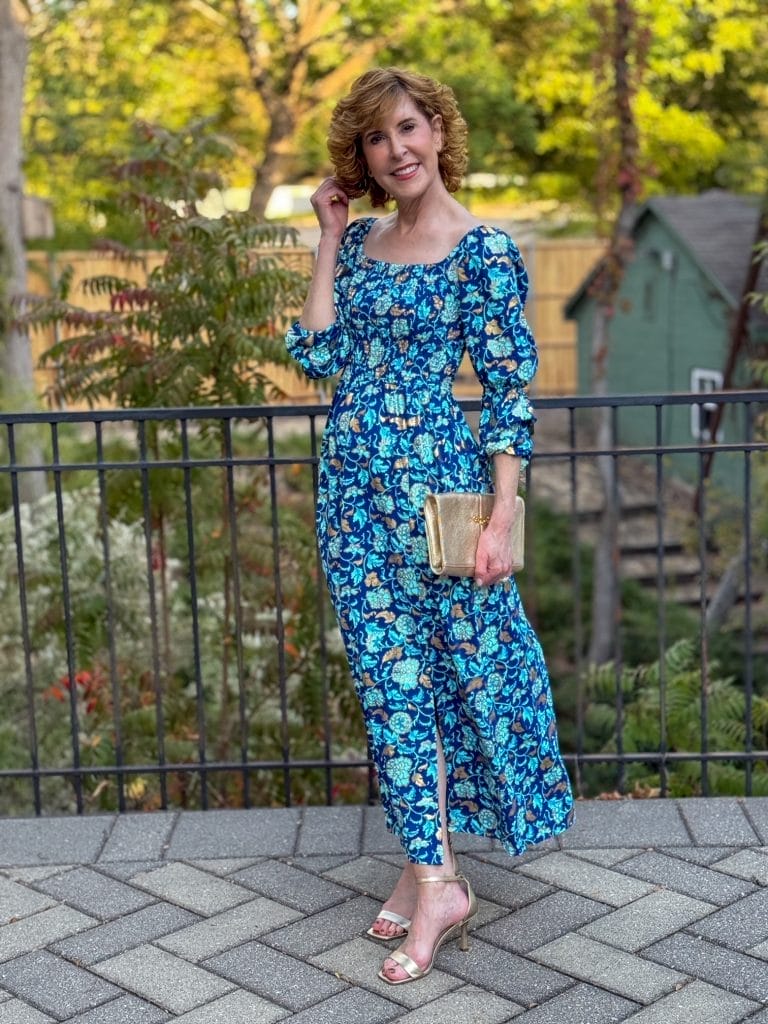 Woman standing outside in a blue and gold cabana life holiday dress holding a gold clutch purse