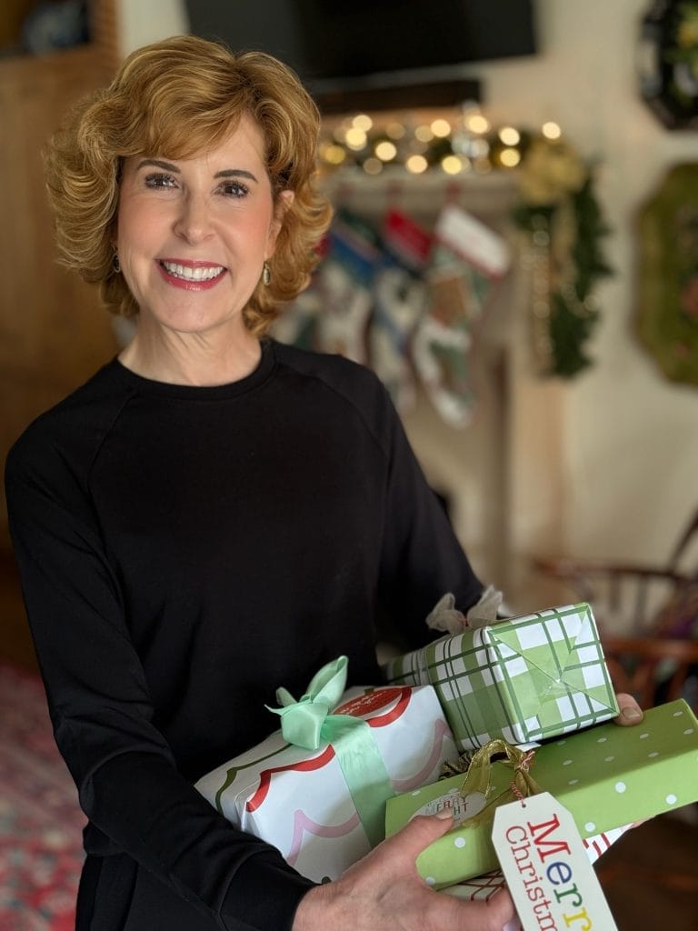 woman holding christmas gifts standing in a living room dressed in a cozy earth crewneck